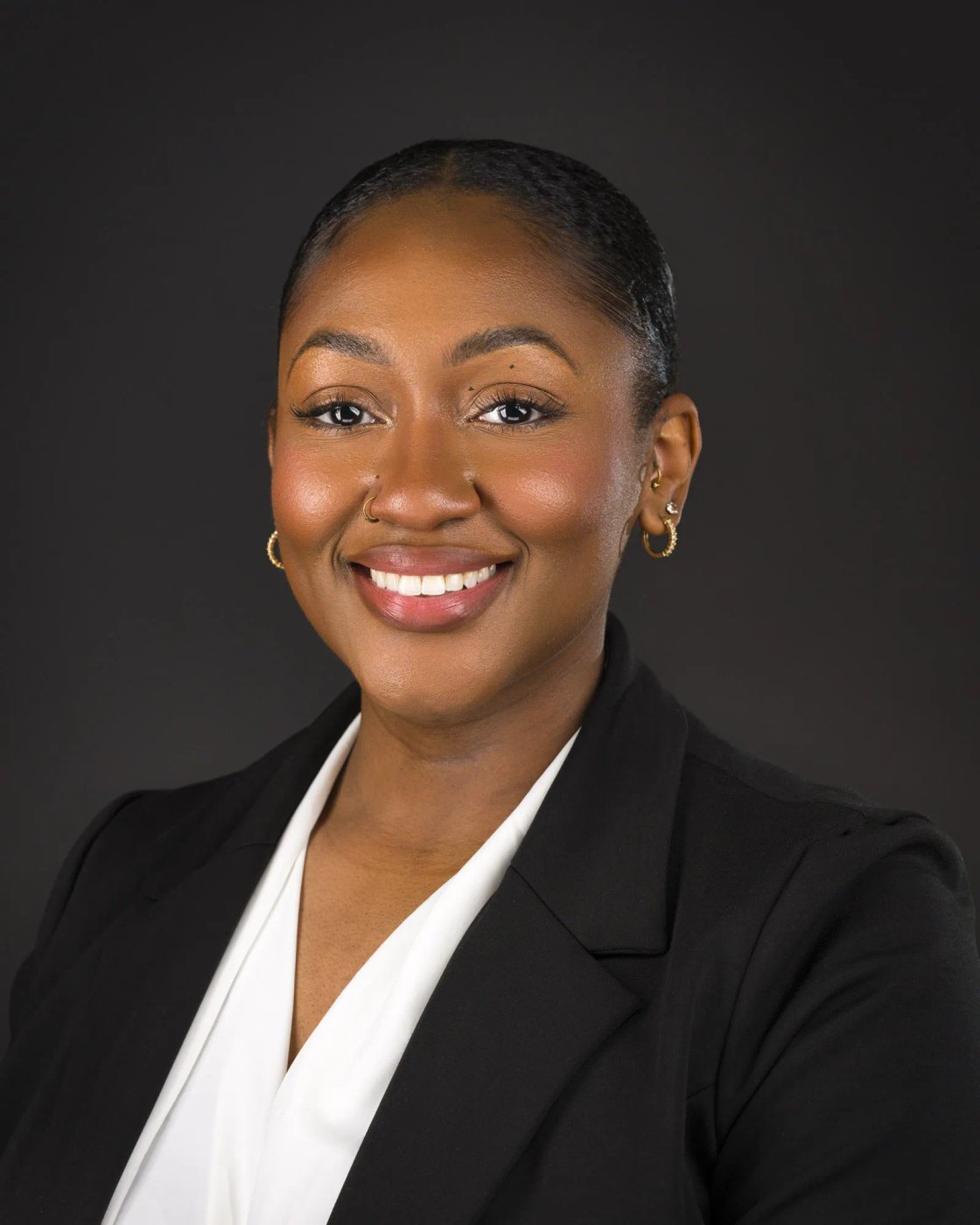 Smiling person in a dark blazer, shown in a close portrait against a plain background