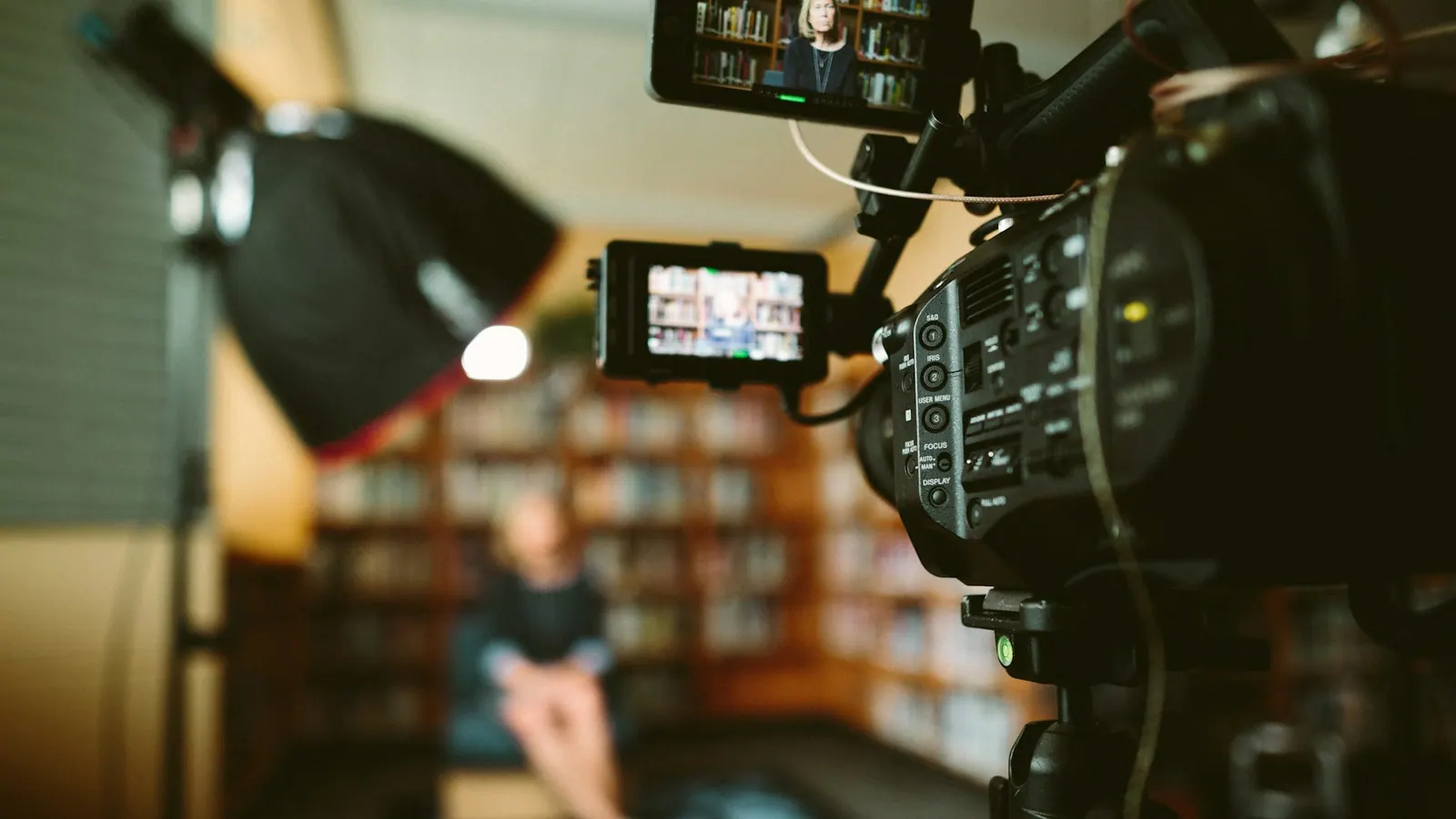 A person seated in front of a bookshelf during filming